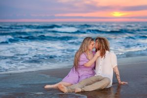 Romantic beach photoshoot with couple sitting in sand during vibrant sunset.