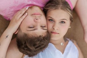 Couple lying close together in intimate portrait on pink background.