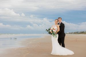 Two people in matching floral dresses walk hand-in-hand along beach at sunset.