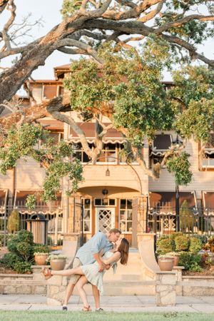 Romantic dip pose in front of a rustic building with beautiful architecture and trees.