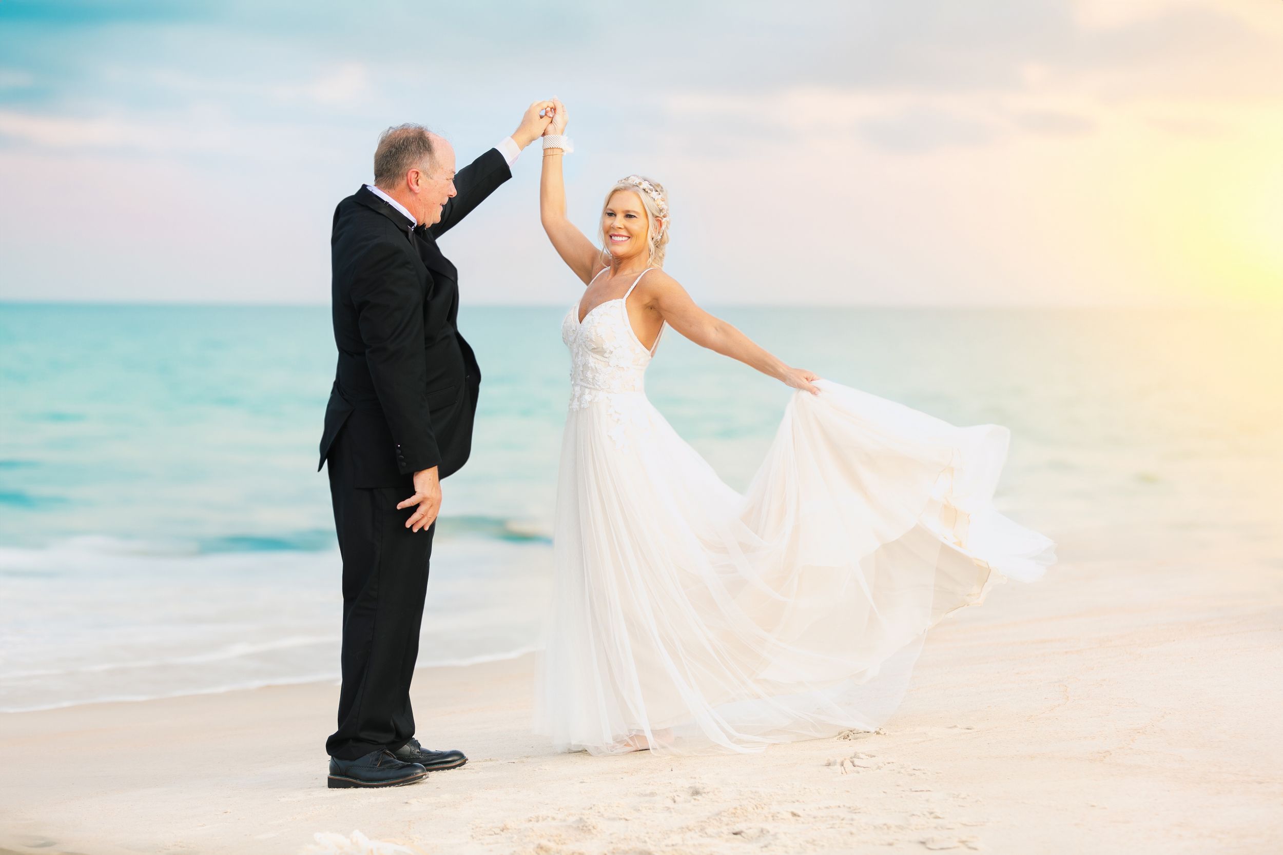 A romantic wedding photo captured at sunset on a beach with flowing white dress and joyful poses.