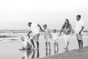 Family holding hands walking along beach shore in black and white.