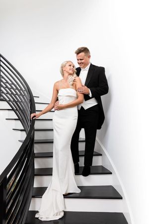 Elegant couple in formal wedding attire pose on modern black and white staircase.