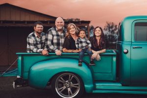 Family in matching plaid shirts posing together in the bed of a classic turquoise pickup truck at sunset.