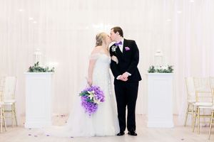 An elegant wedding ceremony setup with white decor and purple bouquet.