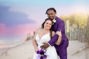 Beach wedding couple portrait with purple and white floral bouquet against sand dunes.