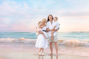A family in white outfits enjoying sunset on a beach with waves.