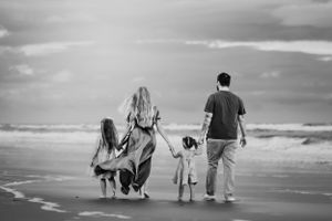 A black and white photo of a family walking on beach with their dog.