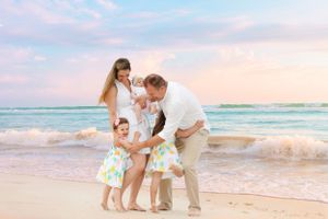 Wedding couple embraces on beach with ocean waves and cloudy sky in background.