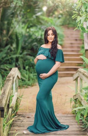 Expectant mother in teal off-shoulder gown poses on garden steps.