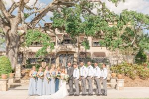 Wedding party in pale blue and grey attire posed together on stone steps.