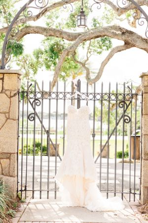 Wedding dress hanging on ornate iron gate framed by curved tree branches and lantern.