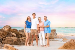 Family of four poses on rocky beach during sunset wearing coordinated blue and white outfits.