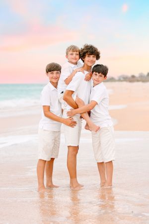 Four siblings in white matching outfits pose together on beach at sunset.
