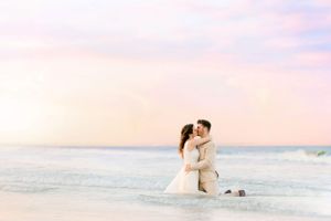 Romantic couple embracing during sunset photoshoot on sandy beach with ocean waves.