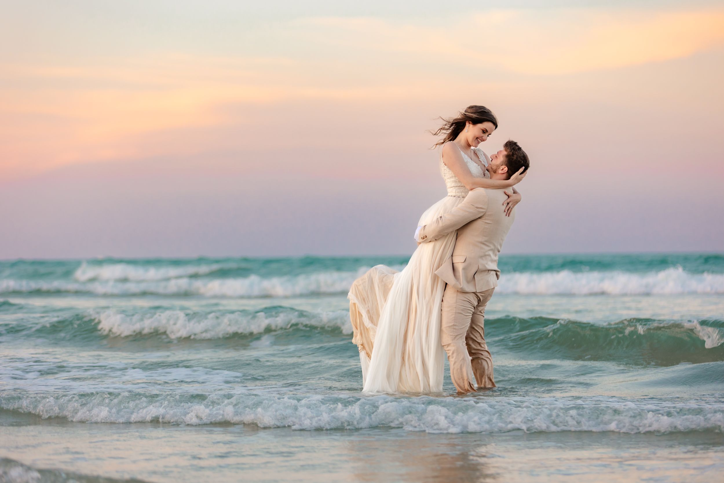 Couple in romantic pose during beach photoshoot at sunset with waves in background.