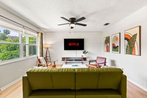 Modern living room with olive green couch, mounted TV, and bright windows overlooking greenery.