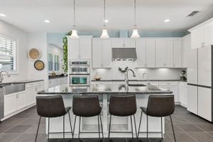 Contemporary white kitchen with dark bar stools and pendant lights over a large center island.