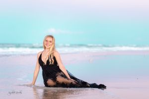 Woman in black dress poses elegantly on beach at sunset.