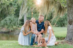 Happy family with dog relaxing together under a tree by a lake.