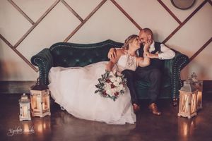 Newlyweds pose on vintage couch with lanterns creating romantic lighting.