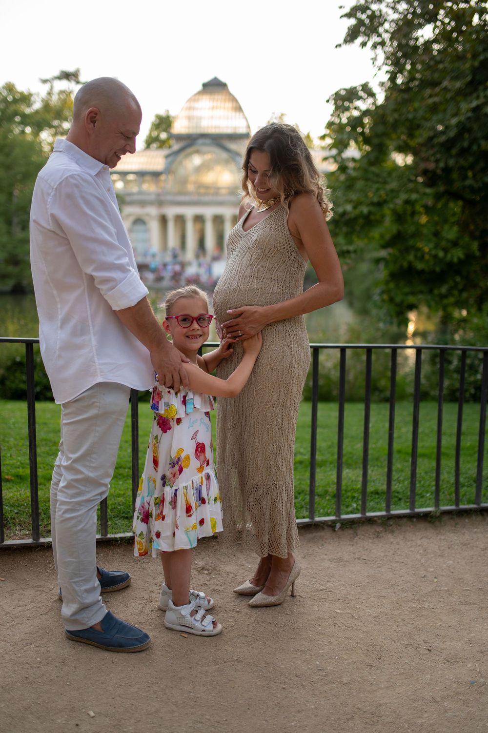 A family shares a tender moment together by an ornate building at sunset in a garden setting.