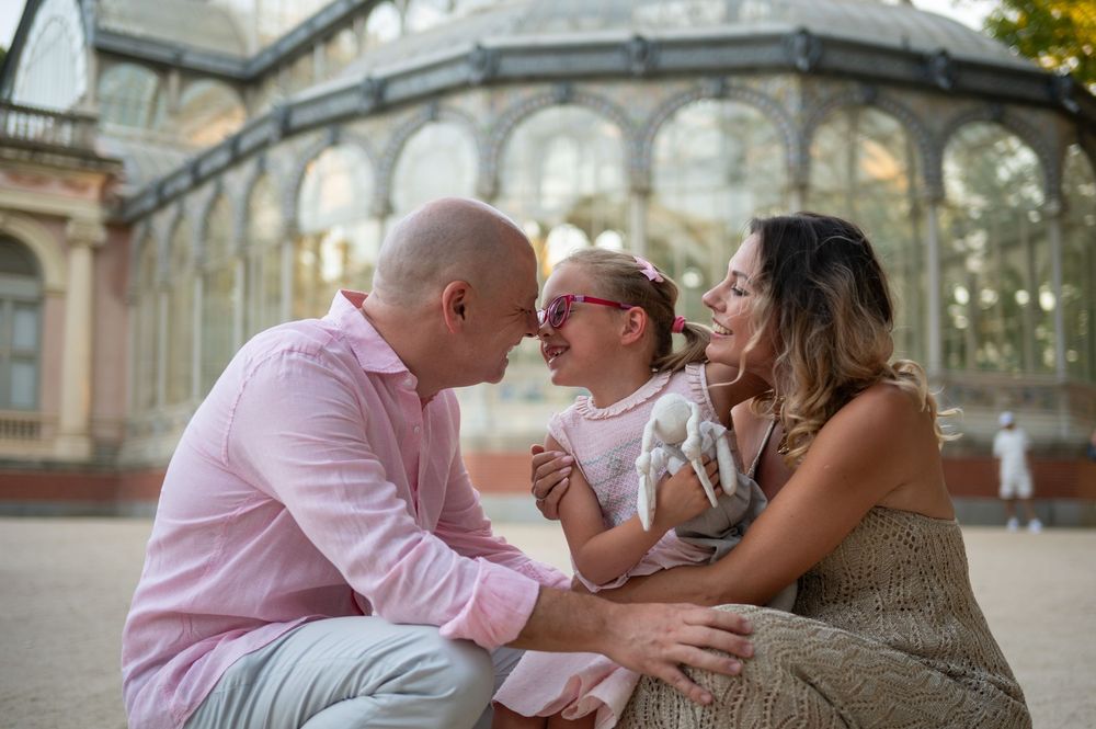A family shares a tender moment together near an ornate glass conservatory building at sunset.