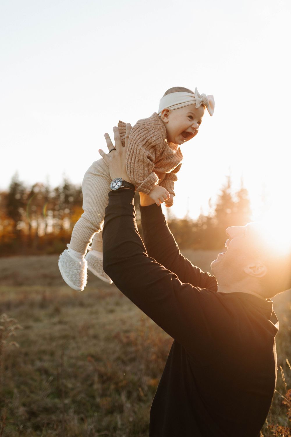 A silhouette of a parent lifting their playful baby against a warm sunset in an autumn field in Guelph Ontario
