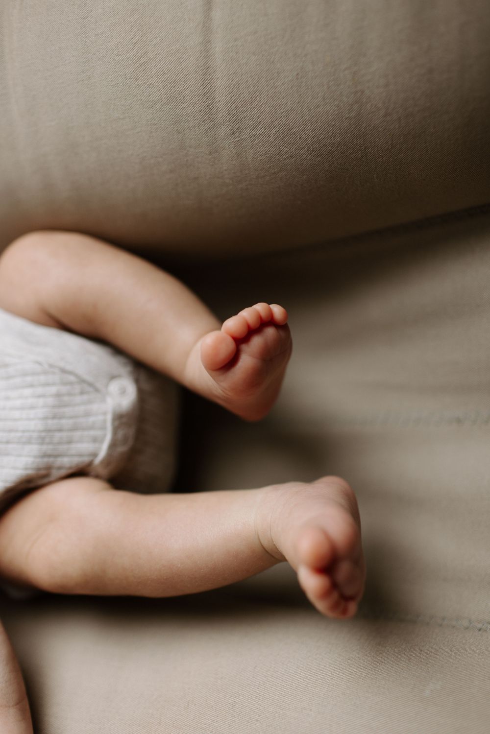 Close-up of tiny baby feet and legs against a beige couch cushion wearing white knit pants in Kitchener Ontario