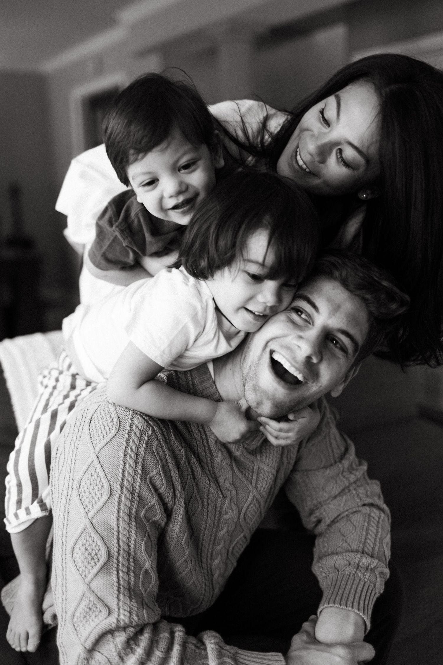 A black and white candid photo showing a joyful family moment as they laugh and embrace together in a natural pose in Toronto Ontario