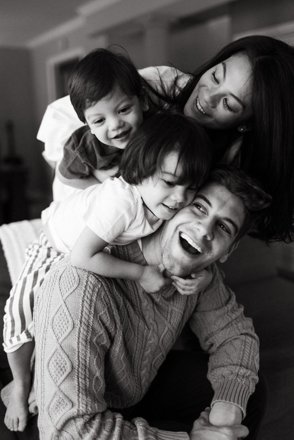 A black and white candid photo showing a joyful family moment as they laugh and embrace together in a natural pose in Toronto Ontario
