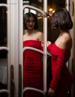 Woman in red ruched dress looks at reflection in elegant mirrored room.