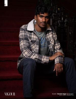 Young man in plaid jacket sits contemplatively on red stairs in moody lighting.