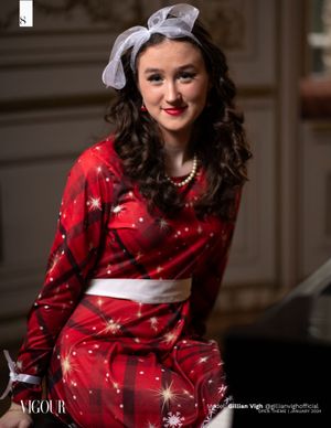 Woman in festive red star-patterned dress and bow headpiece poses in vintage-inspired setting.
