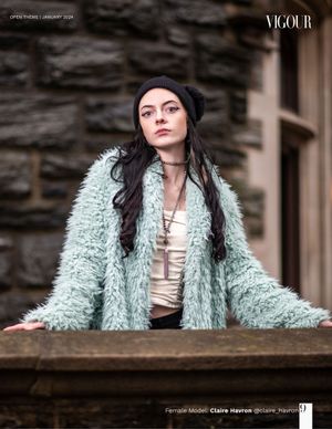 Model wearing mint fuzzy coat and beanie poses against stone building exterior.