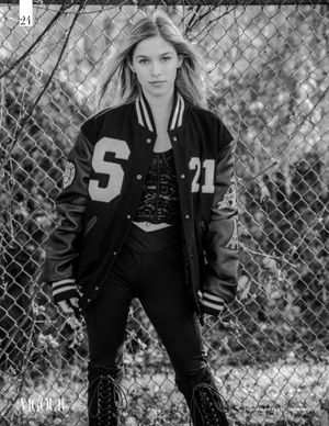 Urban fashion portrait with model wearing varsity jacket against chain link fence.