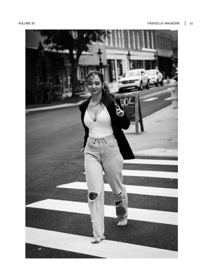 A black and white street photograph shows someone in ripped jeans and a jacket crossing at a crosswalk.