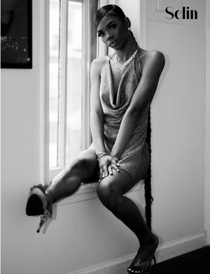 A black and white portrait of a model in a sleek dress posing elegantly by a window.