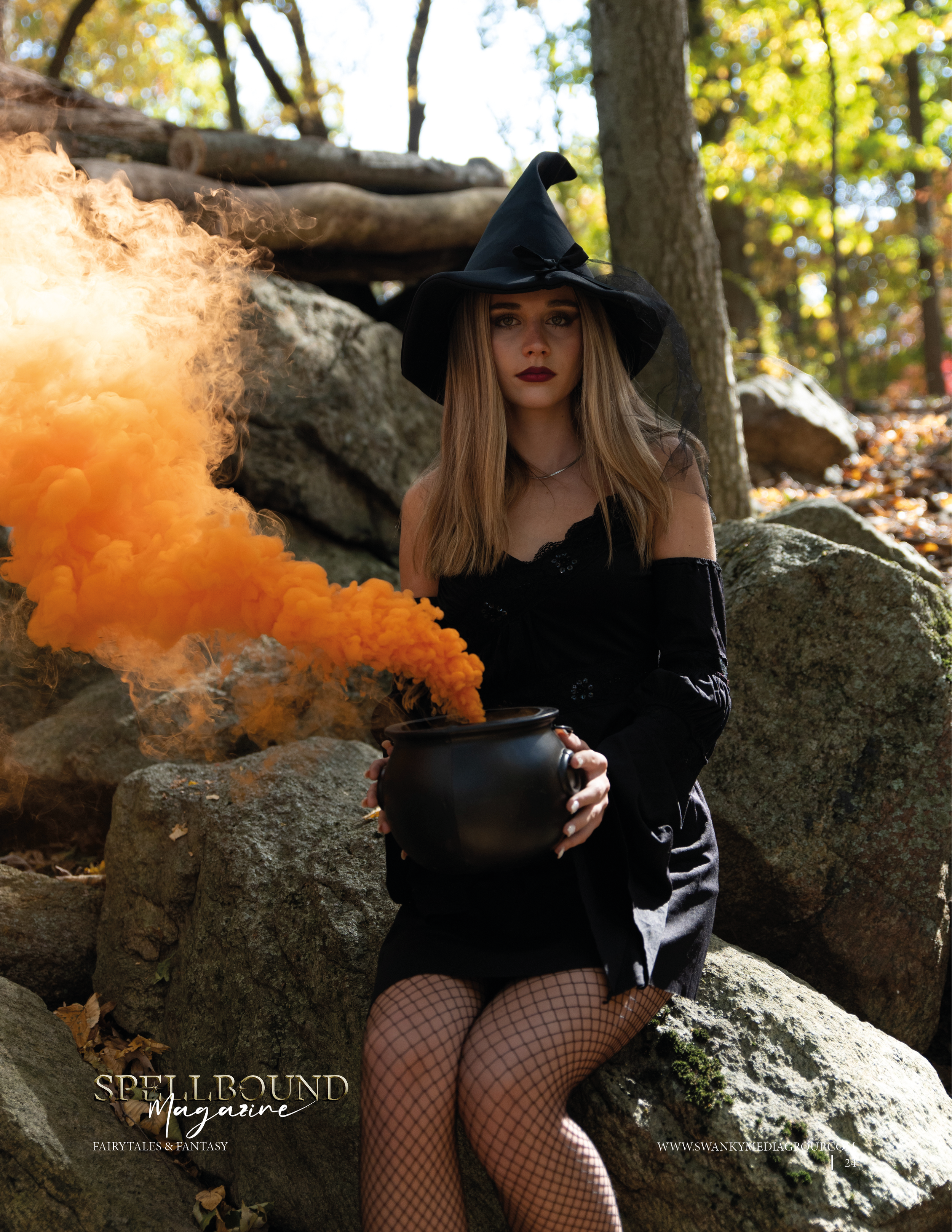 A witch poses on rocky terrain with orange smoke rising from her cauldron in an atmospheric autumn woodland scene.