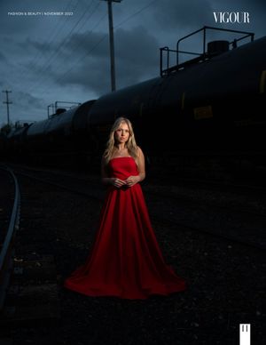 A person in a red evening gown poses dramatically by train tracks at dusk.