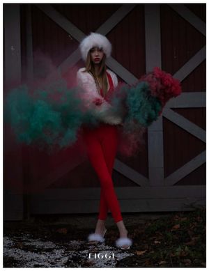 Fashion model in red winter outfit poses against rustic barn door with dramatic green and red smoke effects.