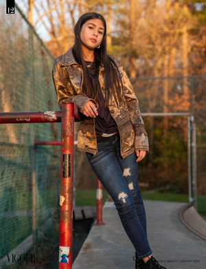 Model wearing gold patterned jacket and distressed jeans leans against red railing during golden hour sunset.
