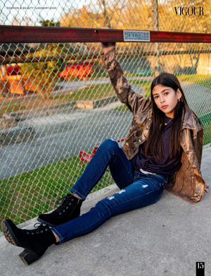 Urban fashion portrait with metallic jacket and combat boots against chain link fence at sunset.