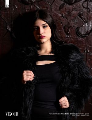 Dark artistic fashion photograph showing a model in black attire with feathered jacket against textured wall backdrop.