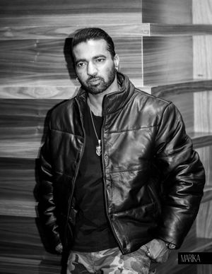Black and white portrait of someone in a leather bomber jacket against a textured wall background.
