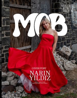 Fashion magazine cover featuring a flowing red evening gown against a rustic stone wall backdrop.