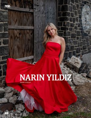 A woman in a flowing red strapless gown poses dramatically against a rustic stone wall backdrop.