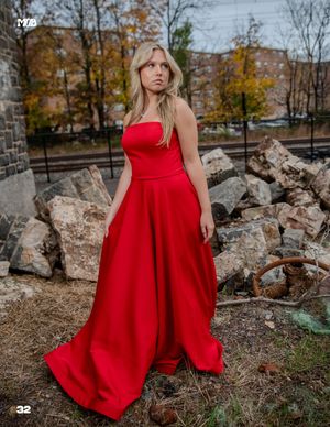 A person in a flowing red ballgown poses among rocky ruins during autumn.