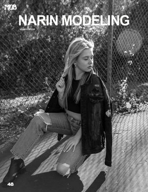 Black and white fashion editorial photo of model in denim jacket against chain link fence.