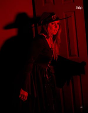 Dramatic red-lit fashion photo featuring model in wide-brimmed hat casting shadow.